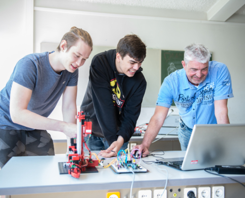 Lehrkraft und Schülergruppe des Leistungskurses Elektrotechnik beim Programmieren eines Mikroprozessors